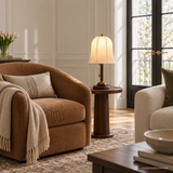 Rora Morrow Wood Table Lamp lit beside a reading chair in a daylight living room