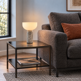 Vian Linden Marble Table Lamp in Grey, glowing on a glass side table beside graphite seating.