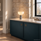 Vian Linden Marble Table Lamp in Grey, glowing on a blue-green cabinet with a stone top.